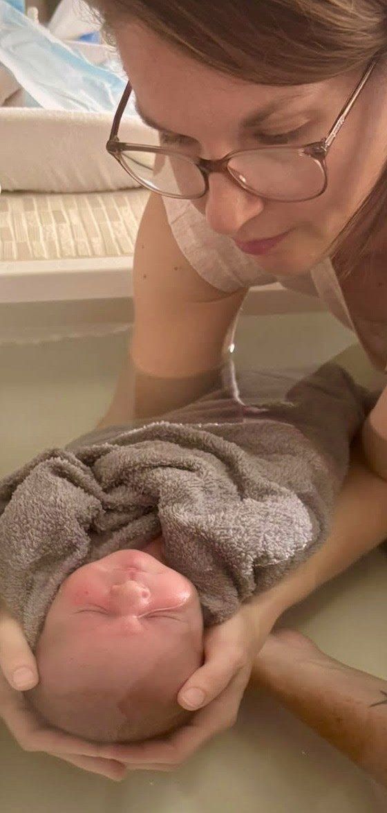 Séverine, sage-femme, penchée sur un nouveau-né emmailloté qu'elle soutient dans le bain