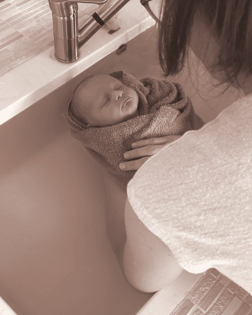 Bébé emmailloté et apaisé, soutenu par Séverine dans le bain